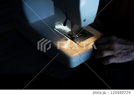 Hands of an older woman threading the sewing machine needle before starting. 120880724