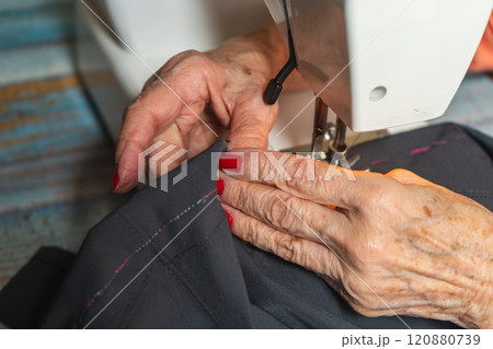 Hands of a female seamstress sewing a pair of pants on a sewing machine. 120880739