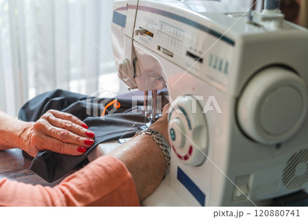 Hands of a female seamstress sewing a pair of pants on a sewing machine. 120880741
