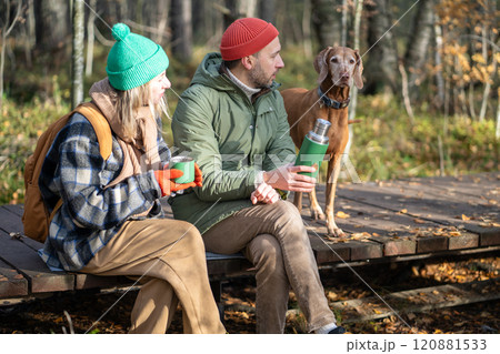 Romantic couple with hunting dog relaxing sitting on wooden path in autumn forest drinking tea. 120881533