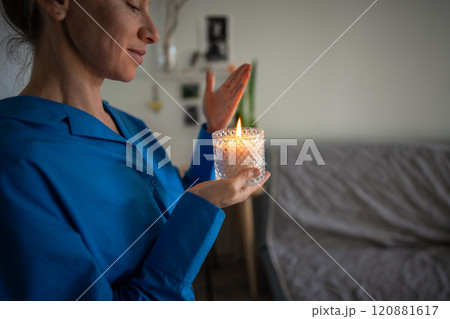 Calm woman enjoy smelling lighted scented candle, meditating, creating cozy atmosphere at home.  120881617