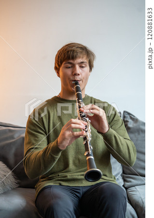 Clarinet player. Man clarinetist playing flute woodwind music instrument sitting on couch at home 120881633