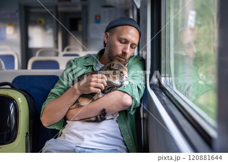 Caring man comforts, hugging nervous cat from carrier, pet on lap watching out window in train car 120881644