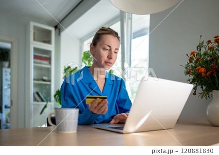 Focused woman on laptop uses credit card for online transaction, lost in heavy spending. Credit debt 120881830