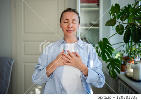Peaceful woman standing with closed eyes, folding one's arms on chest doing breathing exercises. 120881835