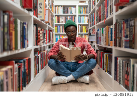 Student african american man reading research textbook in university library sitting on floor. Student african american man reading research textbook in university library sitting on floor. 120881915