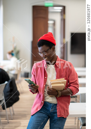 Black student man chatting in social media on smartphone while studying in university library Black student man chatting in social media on smartphone while studying in university library 120881977