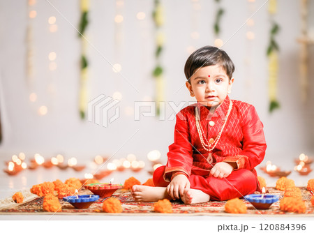 Adorable toddler in traditional red attire celebrating Diwali with festive decor Adorable toddler in traditional red attire celebrating Diwali with festive decor 120884396