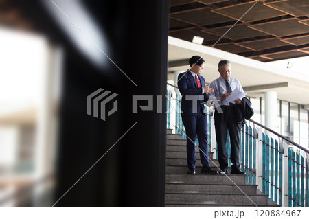 Asian businesspeople having a discussion together while walking inside the office building. Manager is talking with senior manager or chief of management. Businessmen in action portrait. 120884967