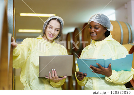 Team of quality control officers are performing the inspection of a beverage container tanks inside the food and beverage factory. Female scientists examine a sample of wine. Team of quality control officers are performing the inspection of a beverage container tanks inside the food and beverage factory. Female scientists examine a sample of wine. 120885059