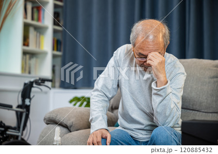 Asian mature old man sitting on sofa headache at home in living room, Depressed senior man unhappy hands rubbing eye suffering from a migraine. Health care 120885432