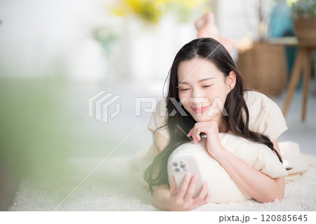 うつ伏せでスマホをタップする美人な女性 明るい白いかわいいイメージ うつ伏せでスマホをタップする美人な女性 明るい白いかわいいイメージ 120885645