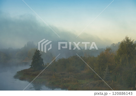Misty morning landscape featuring a tranquil river with trees reflected in the calm water Misty morning landscape featuring a tranquil river with trees reflected in the calm water 120886143