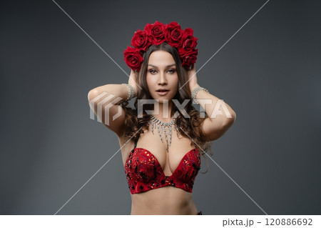 Elegant dancer wearing red outfit and floral crown poses gracefully indoors 120886692