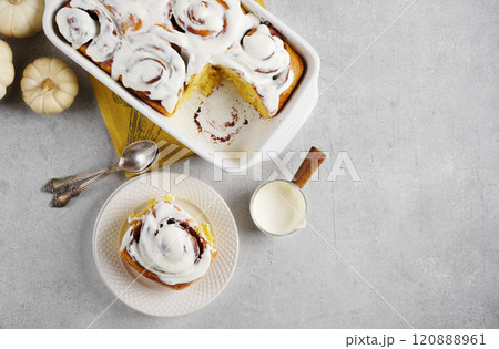 Fragrant freshly baked Cinnamon rolls or cinnabons with pumpkin covered with white cream glaze on the plates on white background. Cinnabons recipe. top view, copy space Fragrant freshly baked Cinnamon rolls or cinnabons with pumpkin covered with white cream glaze on the plates on white background. Cinnabons recipe. top view, copy space 120888961