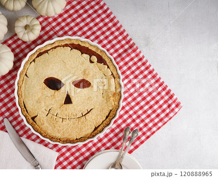 Halloween food. Homemade pumpkin pie or tart with a scary face for Halloween on a red napkin on gray table with cut piece on plate. Copy space. Halloween food concept 120888965