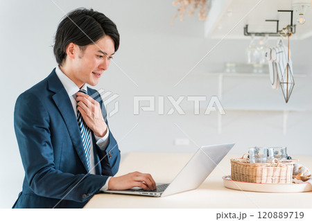 出勤前にダイニングテーブルでノートパソコンで仕事をするスーツ姿の若い男性ビジネスマン 出勤前にダイニングテーブルでノートパソコンで仕事をするスーツ姿の若い男性ビジネスマン 120889719