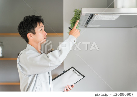 キッチンのレンジフード・換気扇を点検・チェックする作業着姿の男性ビジネスマン 120890907