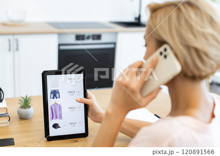 Caucasian woman using tablet and smartphone to shop for clothes online. She is browsing online delivery website, placing order for fashion items. Image focuses on modern technology in everyday life. Caucasian woman using tablet and smartphone to shop for clothes online. She is browsing online delivery website, placing order for fashion items. Image focuses on modern technology in everyday life. 120891566