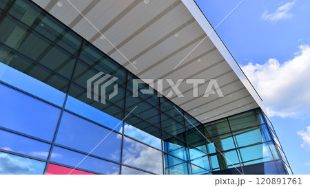 Fragment of a modern building made of steel and glass. Abstract modern commercial architecture fragment. Walls made of shiny glass and steel under blue sky. 120891761