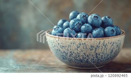 A bowl filled with fresh blueberries, showcasing their rich blue color and vibrant texture, set against a softly blurred background. 120892465