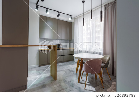 Modern kitchen in a small cozy contemporary studio apartment. Table and chairs in the foreground. Built in household appliance 120892788