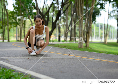Cheerful young woman adjusting her sneakers before starting her fitness routine in the park Cheerful young woman adjusting her sneakers before starting her fitness routine in the park 120893722