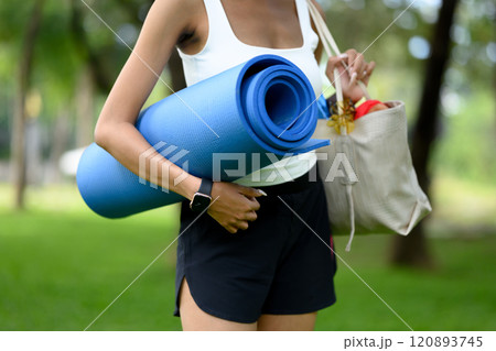 Woman carrying yoga mat and tote bag filled with workout items preparing for an outdoor exercise session Woman carrying yoga mat and tote bag filled with workout items preparing for an outdoor exercise session 120893745