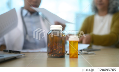 Close up of medicine bottles on wooden table with doctor and patient consulting in the background 120893765