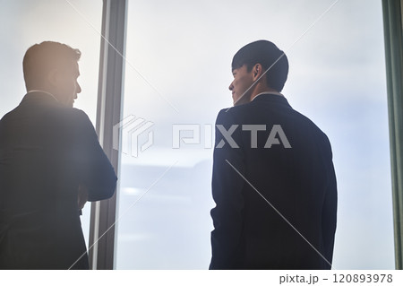 two asian businesspeople talking chatting standing by the window talking chatting in office 120893978