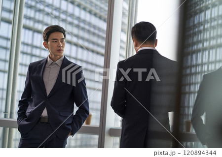 two asian businesspeople talking chatting standing by the window talking chatting in office two asian businesspeople talking chatting standing by the window talking chatting in office 120894344