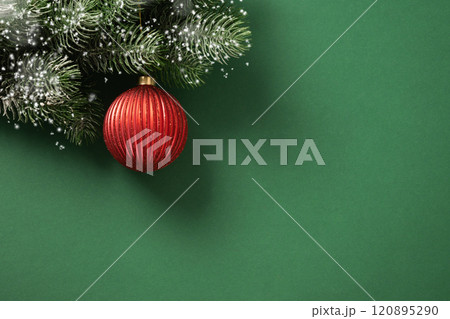 Christmas red bauble on fir snowy branches on green background. Xmas greeting card. New Year banner. Copy space. View from above. 120895290