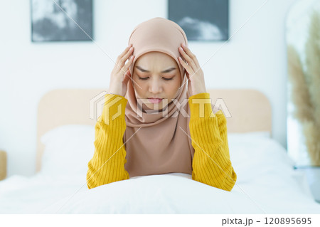 Unhappy - stressful Asian young muslim woman sitting alone on the bed in the morning. Asian muslim woman having a mental burn out or depression problem from working and social environment. 120895695