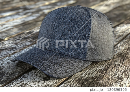 A denim cap is placed on an aged wooden surface, showcasing its fabric texture and casual design. The natural light highlights the details of the cap, emphasizing its stylish appeal. 120896596
