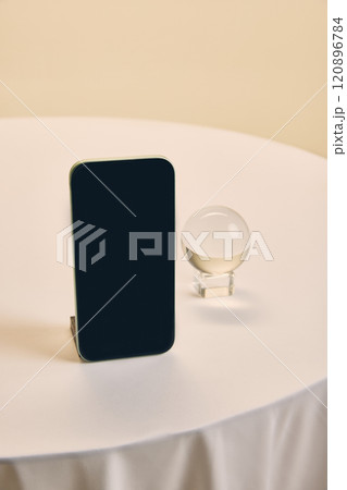 Smartphone displayed upright beside transparent crystal globe on white table, offering minimal and versatile mockup for business themes. 120896784