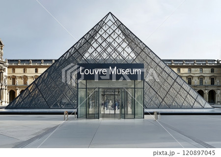 The glass pyramid entrance of the Louvre Museum stands tall in Paris, showcasing modern architecture against classic buildings on a clear day. Visitors can explore art and history inside. 120897045