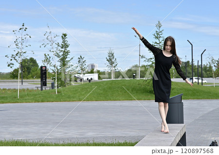 Woman balancing barefoot outdoors on a park pathway on a sunny day. 120897568