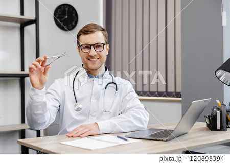 Young attractive otolaryngologist doctor sitting at his workplace in the office and holding a nose mirror 120898394