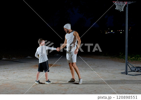 A young man and a boy shake hands before playing basketball in the evening in the park A young man and a boy shake hands before playing basketball in the evening in the park 120898551