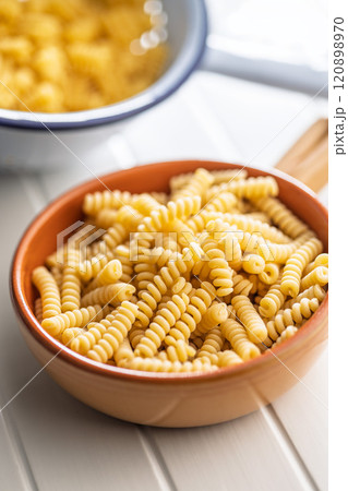 Uncooked italian pasta. Fusilli pasta in bowl on white table. 120898970