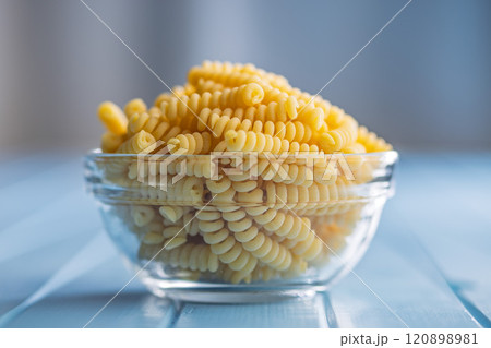Uncooked italian pasta. Fusilli pasta in bowl on blue table. 120898981