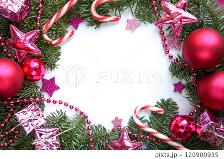 Vibrant Christmas-themed photograph features lush green fir branches adorned with fuchsia ornaments, candy canes, pink stars, shiny beads and small wrapped gifts, framing a blank white center for text 120900935