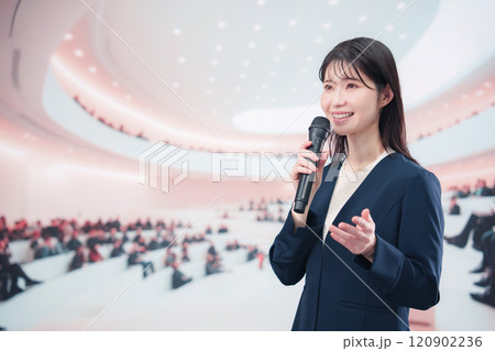 ホールで司会・プレゼンをするスーツを着た若い女性 ホールで司会・プレゼンをするスーツを着た若い女性 120902236