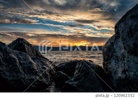 Large blocks of stones on the shore of the lake against the backdrop of a beautiful sunset 120902332