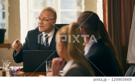 Senior businessman shares ideas and insights with colleagues during formal meeting, fostering teamwork and collaboration. Senior businessman shares ideas and insights with colleagues during formal meeting, fostering teamwork and collaboration. 120903669