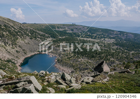 Summer day in low mountains. Stone hillsides, evergreen conifers, rocks in distance and emerald colored lake. Summer day in low mountains. Stone hillsides, evergreen conifers, rocks in distance and emerald colored lake. 120904346