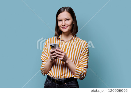 Young smiling woman using smartphone looking at camera in blue background Young smiling woman using smartphone looking at camera in blue background 120906093