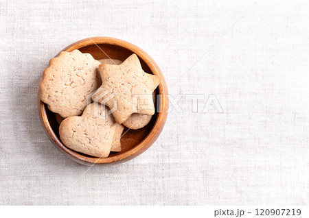 Homemade gingerbread cookies in a wooden bowl on linen fabric, with empty space for text. Sweet, light brown and flat baked goods for Christmas, flavored with ginger, cloves, nutmeg, and cinnamon. 120907219