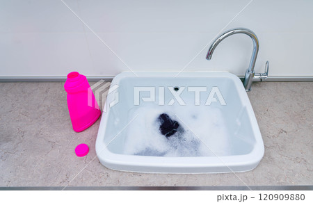 Hand-washing clothes with detergent in a sink filled with soapy water. 120909880