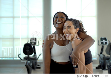 Professional Hispanic exercise and fitness trainer teaching African - American Black ethnic woman doing a muscle stretching in the indoor gym. Women practicing an exercise in fitness club together. Professional Hispanic exercise and fitness trainer teaching African - American Black ethnic woman doing a muscle stretching in the indoor gym. Women practicing an exercise in fitness club together. 120911956